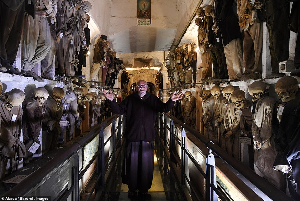 One of the monks who watches over the mummies walks down a hall full of them stacked either side as he shows people around