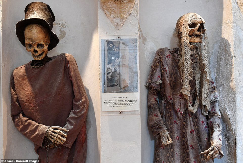 This images shows one corpse wearing a top hat, while the other one wears a floral dress and a lace head ensemble