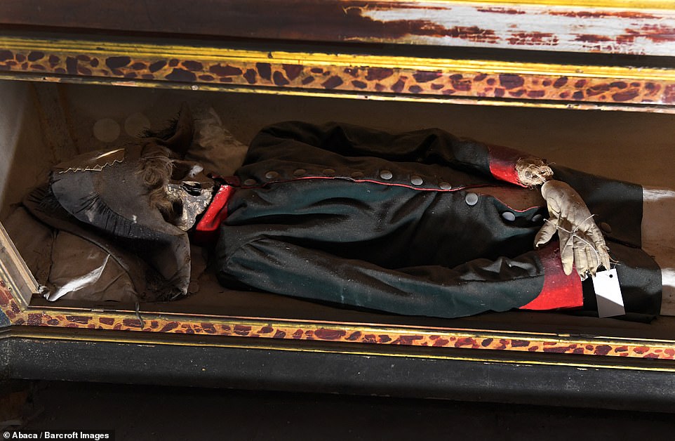 The corpses are now watched over by a group of monks. This corpse seems to have been left in a military style outfit, and some curled hair can be seen poking out of a hat